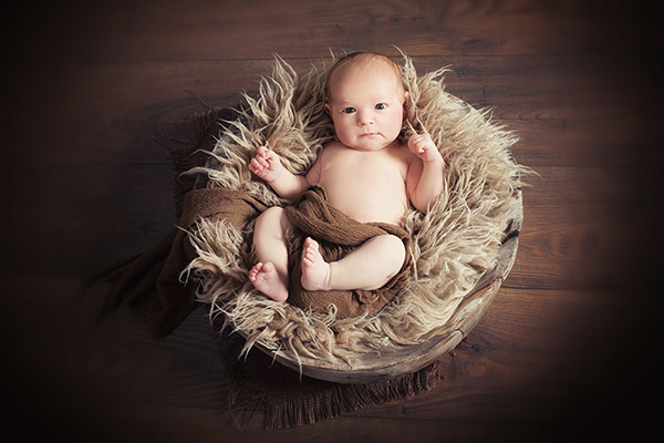 Babyfotografin Düsseldorf fotografiert Baby von oben. Das baby liegt in Holzschale und beobachtet mit wachem Blick das Geschehen. 