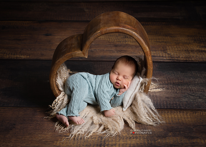 Babyshooting in Düsseldorf: Baby liegt auf kuscheliger Decke in hölzerner Herzform. Fotografin: Aleksandra Ola Karlowski. Fotoatelier in Düsseldorf-Benrath.