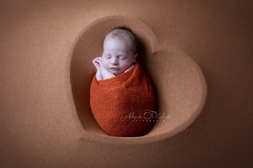 Baby liegt nach Pucken friedlich schlafend in einer herzförmigen Schüssel auf weichem Stoff. Fotografin A. Ola Karlowski
