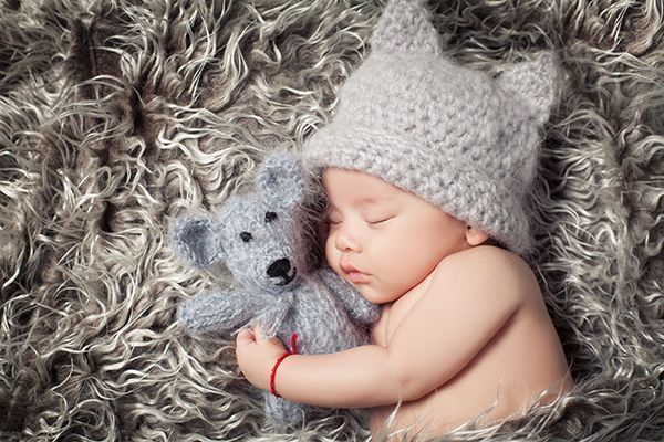 Verspielte Neugeborenenfotografie im Studio in Düsseldorf: schlafendes Baby mit Strickmütze und Kuscheltier auf weicher Decke