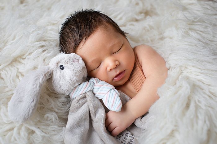 Neugeborenenfoto im Studio in Düsseldorf: schlafendes Baby kuschelt mit Stoffhasen auf weicher Decke