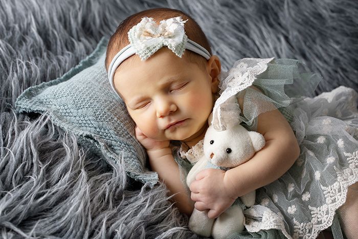 Verspielte Neugeborenenfotografie im Studio in Düsseldorf: schlafendes Baby im Kleid mit Kuscheltier auf weicher Decke