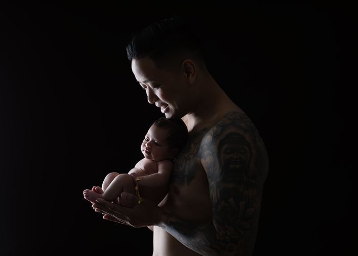 Babyfotografie mit Vater im Studio in Düsseldorf – Neugeborenes liegt geborgen in den Händen des Vaters vor dunklem Hintergrund
