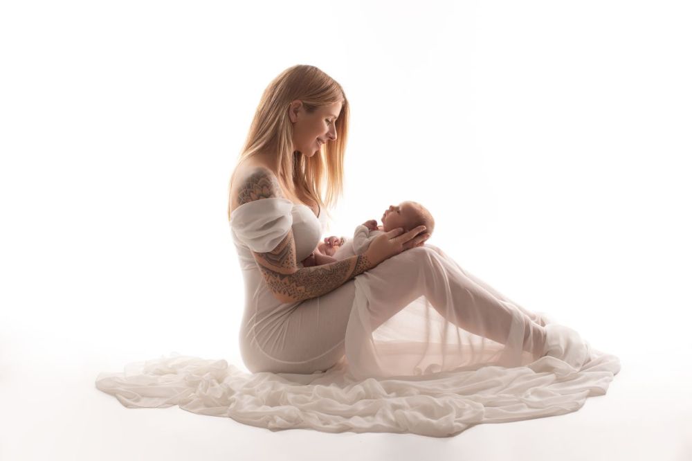 Babyfotografie mit Mutter im Studio in Düsseldorf – Neugeborenes liegt geborgen im Arm vor hellem Hintergrund
