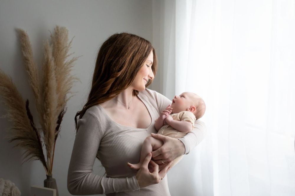 Babyfotografie mit Mutter im Studio in Düsseldorf – Neugeborenes wird liebevoll im weichen Fensterlicht gehalten