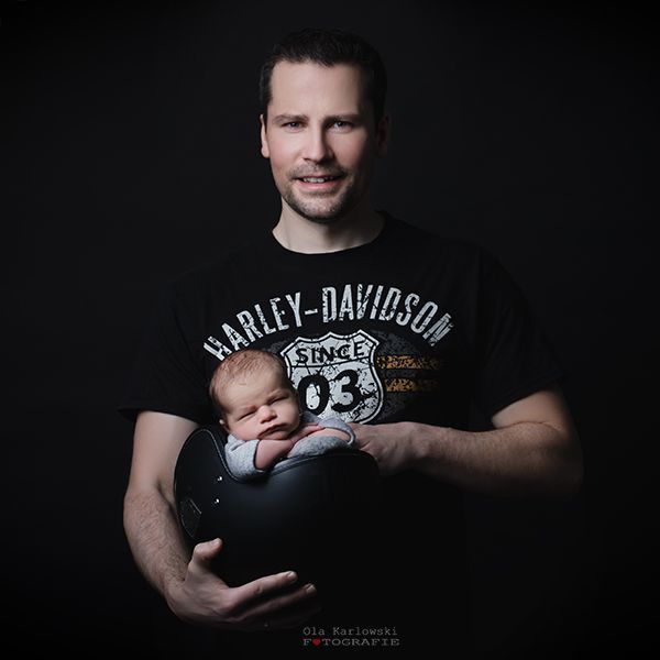 Babyfotografie mit Vater im Studio in Düsseldorf – Neugeborenes liegt geborgen im Arm seines Vaters vor dunklem Hintergrund