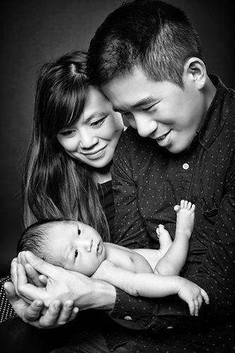 Schwarzweiß Babyfoto im Studio Düsseldorf: Eltern halten ihr Neugeborenes liebevoll in den Händen und blicken es ruhig an