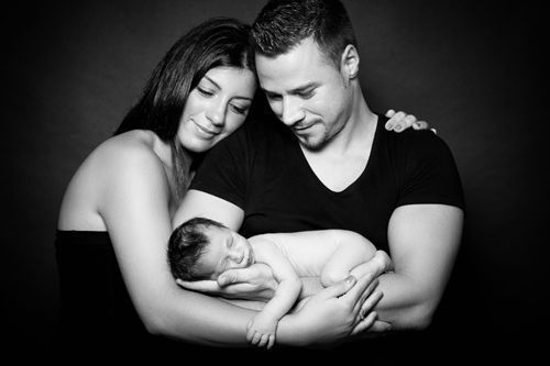 Schwarzweiß Babyfoto im Studio Düsseldorf: Eltern halten ihr schlafendes Neugeborenes gemeinsam liebevoll im Arm