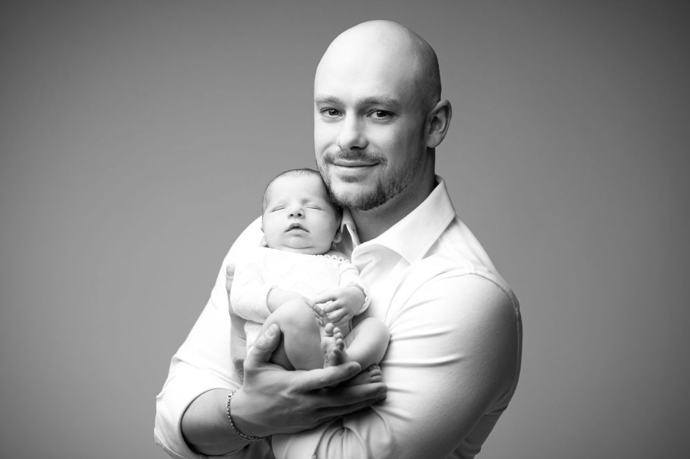 Schwarzweiß Babyfoto im Studio Düsseldorf: Vater hält sein schlafendes Neugeborenes liebevoll im Arm