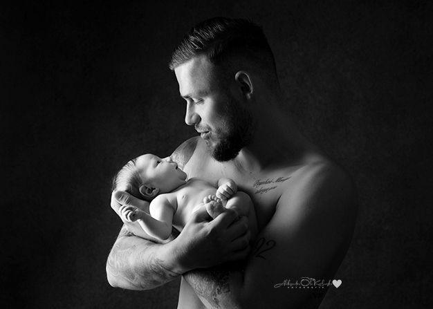 Schwarzweiß Babyfoto im Studio Düsseldorf: Vater hält sein Neugeborenes liebevoll im Arm und blickt es ruhig an